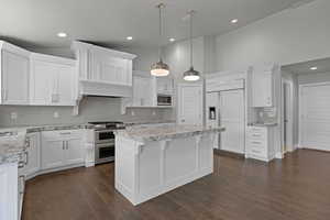 Kitchen featuring built in appliances, backsplash, white cabinetry, recessed lighting, and a high ceiling