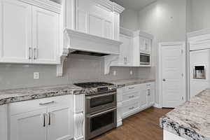 Kitchen featuring built in appliances, decorative backsplash, dark wood-style flooring, and white cabinets