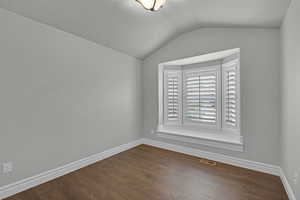 Spare room with dark wood-type flooring and vaulted ceiling