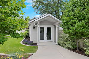 View of exterior entry featuring french doors, stucco siding, and a lawn