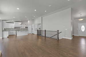 Unfurnished living room with high vaulted ceiling, recessed lighting, and dark wood-style flooring