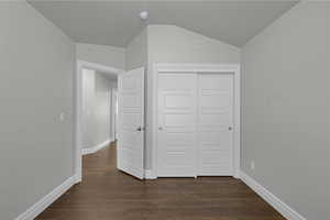 Unfurnished bedroom with dark wood finished floors, a closet, and lofted ceiling