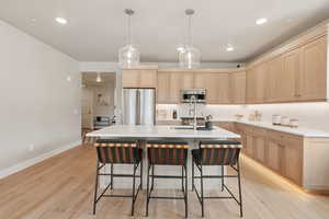 Kitchen with light brown cabinetry, freestanding refrigerator, light wood-type flooring, light countertops, and a breakfast bar area