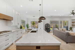 Kitchen featuring stainless steel gas stovetop, an island with sink, open floor plan, a ceiling fan, and decorative backsplash