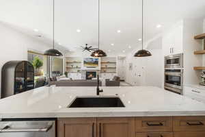 Kitchen with stainless steel appliances, a center island with sink, open floor plan, open shelves, and a glass covered fireplace