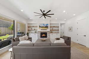 Living room featuring a ceiling fan, light wood-type flooring, a glass covered fireplace, and recessed lighting