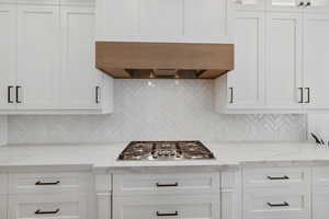 Kitchen featuring extractor fan, stainless steel gas stovetop, white cabinetry, and backsplash