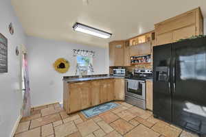 Kitchen featuring stainless steel appliances, open shelves, dark countertops, stone tile flooring, and decorative backsplash
