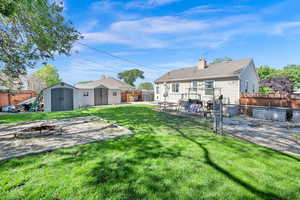 Back of house with a storage unit, a fire pit, a fenced backyard, and a patio area