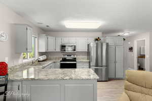 Kitchen with stainless steel appliances, a peninsula, light wood-type flooring, light stone counters, and a textured ceiling
