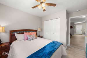 Bedroom with light wood-style floors, a closet, ceiling fan, and a textured ceiling