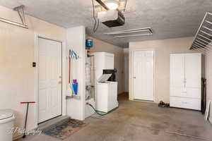 Garage featuring estacked washer and dryer, a garage door opener, and a textured wall