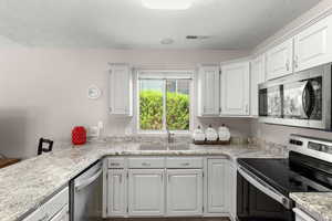 Kitchen with stainless steel appliances, white cabinets, a textured ceiling, and light stone counters