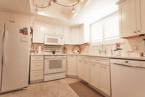 Kitchen with white appliances, backsplash, light countertops, light tile patterned flooring, and white cabinetry