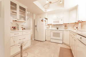 Kitchen with white appliances, backsplash, a tray ceiling, and light countertops