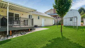 View of green lawn with a wooden deck and a storage unit
