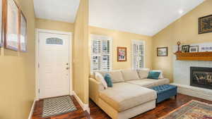 Foyer entrance with dark wood-type flooring, plenty of natural light, vaulted ceiling, and a brick fireplace