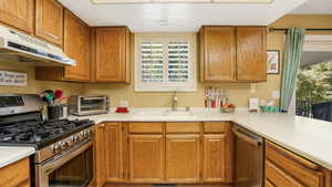Kitchen with stainless steel appliances, under cabinet range hood, light countertops, and brown cabinetry