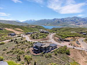 Modern hillside residence featuring multiple balconies, a flat roofline, and extensive glass doors, all set against a backdrop of a large body of water and distant snow-capped mountains