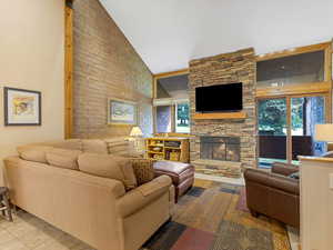 Living room with high vaulted ceiling, plenty of natural light, and a large stone fireplace