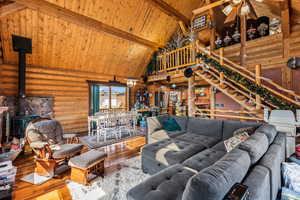 Living room with a wooden ceiling with exposed beams, high vaulted ceiling, a wood stove, hardwood flooring, and log walls