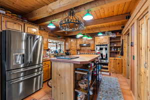 Kitchen featuring appliances with stainless steel finishes, tile counters, light tile patterned flooring, a wooden ceiling with exposed beams, and a center island