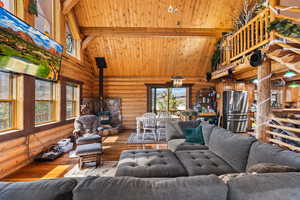 Living area featuring rustic walls, high vaulted ceiling, a wood stove, and hardwood flooring
