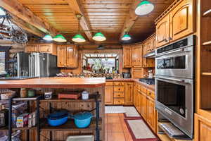 Kitchen with appliances with stainless steel finishes, a wood ceiling with exposed beams, light tile patterned floors, tile countertops, and under cabinet range hood