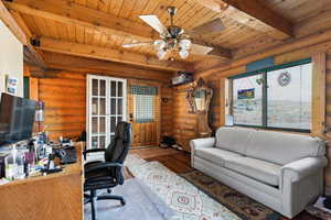 area featuring a wood ceiling with exposed beams, rustic walls, ceiling fan, and wood finished floors