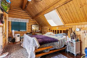Bedroom featuring log walls, hardwood / wood-style floors, a wood ceiling with exposed beams, and high vaulted ceiling