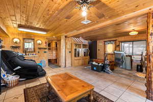 Tiled living area featuring wood ceiling, wooden walls, and ceiling fan