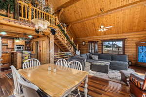 Dining room with rustic walls, a wooden ceiling with exposed beams, high vaulted ceiling, stairs, and dark hardwood floors