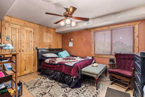 Bedroom featuring light tile patterned flooring, wood walls, and ceiling fan