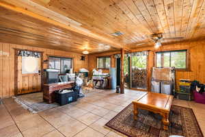 Living room with wood ceiling, wood walls, plenty of natural light, light tile patterned flooring, and a ceiling fan