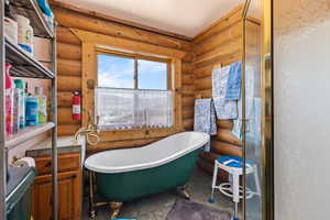 Full bathroom featuring log walls and a freestanding bath