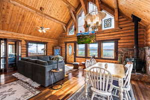 Dining space featuring a wood stove, high vaulted ceiling, a wood ceiling with exposed beams, log walls, and hardwood  floors