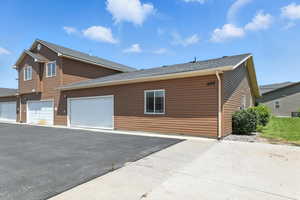 View of property exterior featuring asphalt driveway, a garage, and a shingled roof
