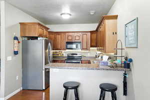 Kitchen with appliances with stainless steel finishes, a peninsula, dark wood-style flooring, a breakfast bar area, and a textured ceiling