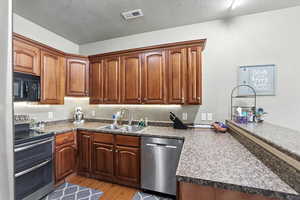 Kitchen with stainless steel appliances, a peninsula, light wood-style floors, a textured ceiling, and dark countertops