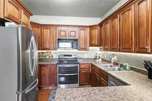 Kitchen with stainless steel appliances, dark wood-style flooring, brown cabinets, and a textured ceiling