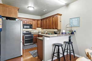 Kitchen with appliances with stainless steel finishes, a peninsula, a kitchen breakfast bar, dark wood-type flooring, and a textured ceiling