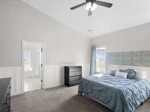 Bedroom with carpet, wainscoting, high vaulted ceiling, ensuite bath, and a ceiling fan
