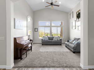 Carpeted living area with high vaulted ceiling, arched walkways, ceiling fan, wood finished floors, and recessed lighting