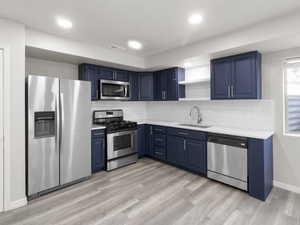 Kitchen with appliances with stainless steel finishes, blue cabinets, open shelves, light countertops, and light wood-style floors