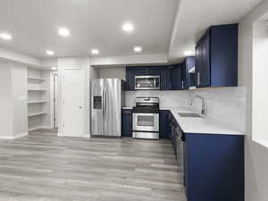 Kitchen featuring appliances with stainless steel finishes, blue cabinetry, open shelves, light countertops, and recessed lighting