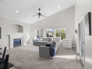 Carpeted living room with high vaulted ceiling, a ceiling fan, a tile fireplace, and recessed lighting