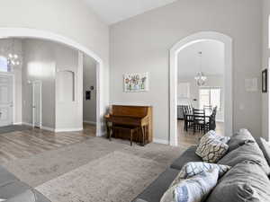 Living room with a chandelier, arched walkways, high vaulted ceiling, and wood finished floors