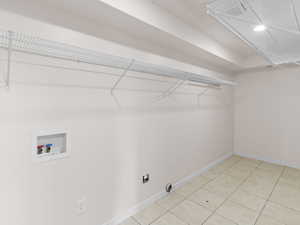 Washroom with hookup for a washing machine, light tile patterned floors, and hookup for an electric dryer