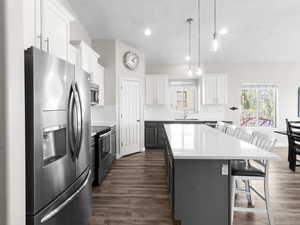 Kitchen with appliances with stainless steel finishes, a center island, a breakfast bar area, dark wood-type flooring, and light countertops
