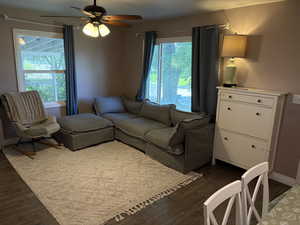 Living area with dark wood-type flooring, healthy amount of natural light, and ceiling fan